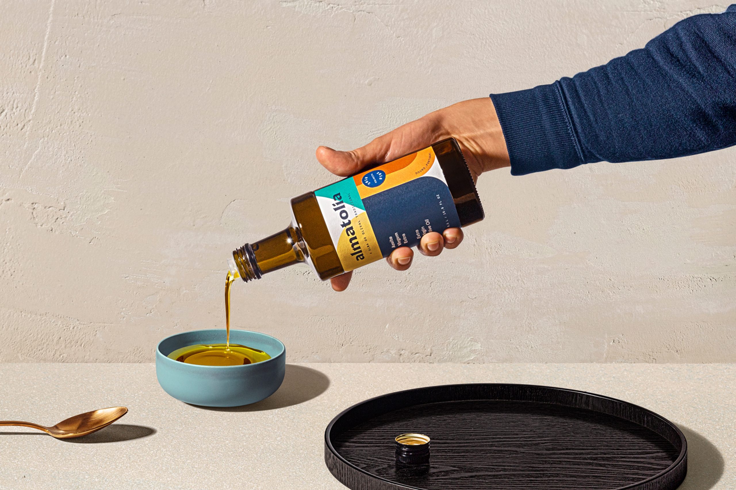 Hand pouring olive oil, showcasing Almatolia label.